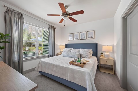Bedroom with a wood-blade ceiling fan, an upholstered headboard, carpet and a window with blinds and curtains.