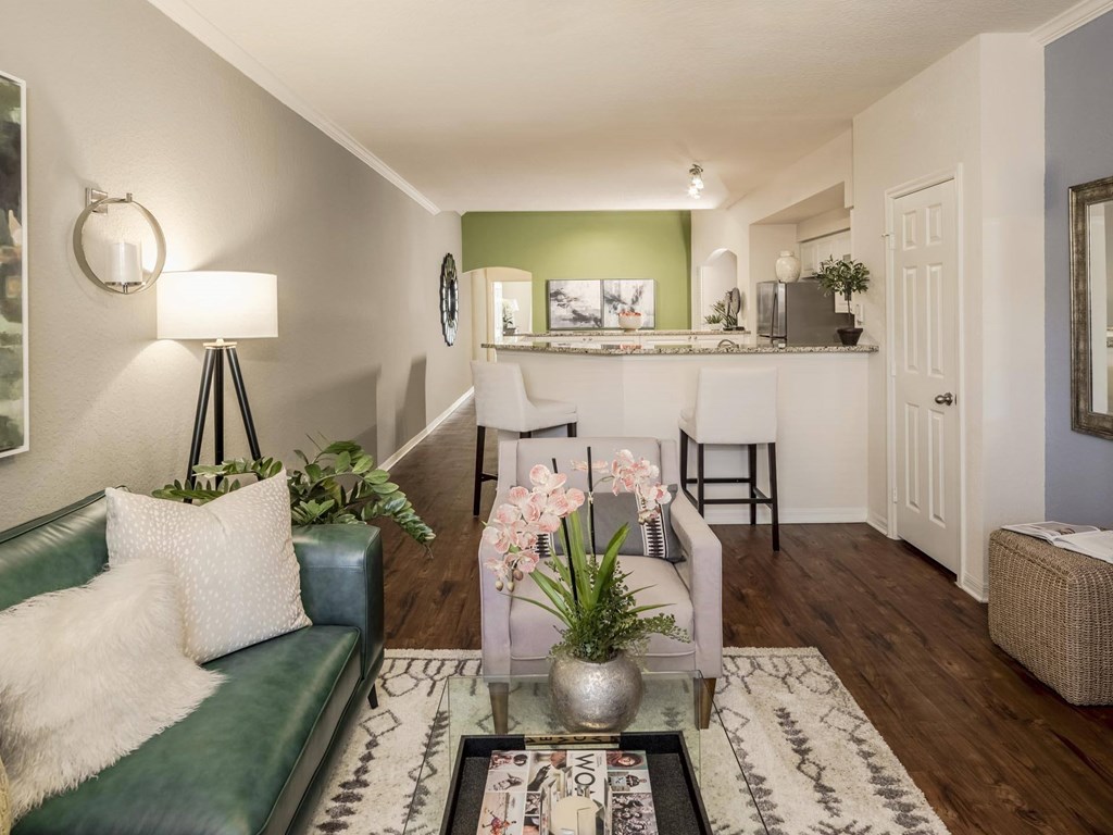 Open living area with bar seating and wood floors leading to the kitchen