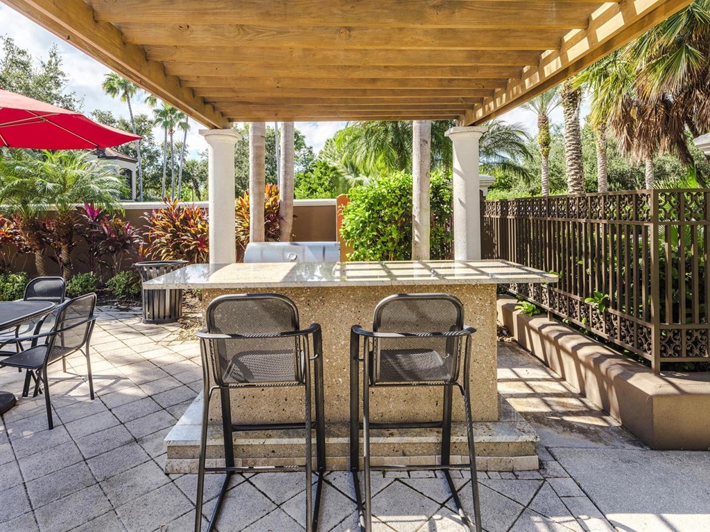 Outdoor grilling station under a pergola with bar seating and tropical landscaping