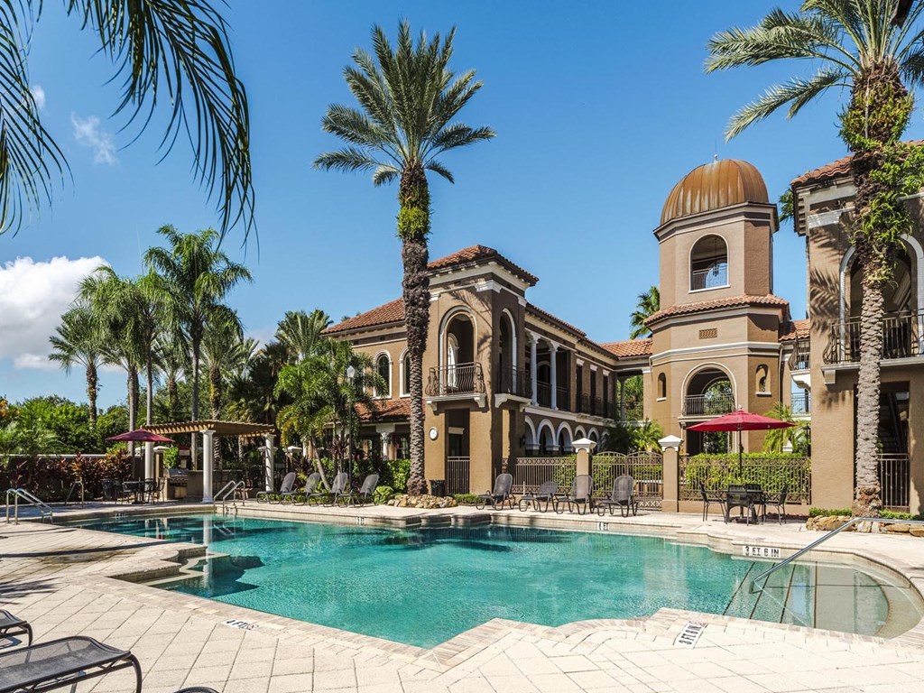 Palm-lined pool with shaded seating and arched building backdrops