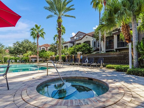 Circular brick-rimmed spa set into the paver deck, with the main pool, loungers and tall palms in the background.