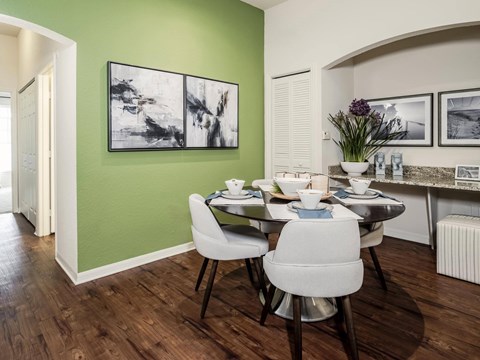Dining area with an oval table, four upholstered chairs, a granite ledge and two framed prints on a green wall.