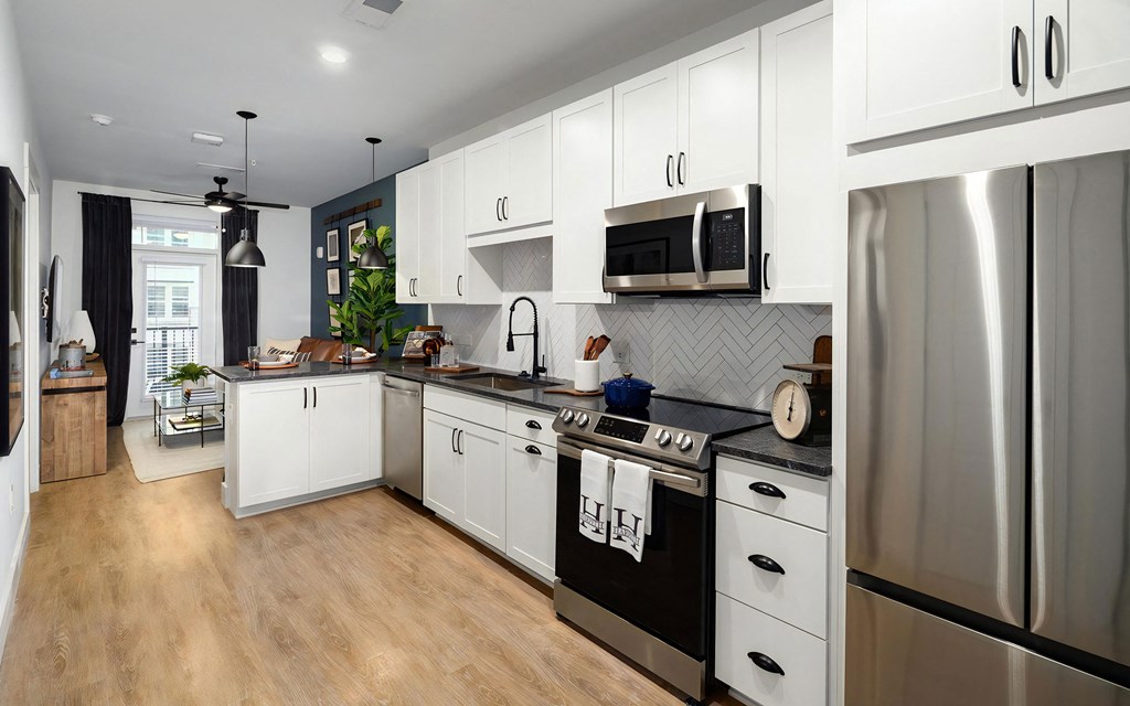 Galley-style kitchen with stainless steel appliances, white cabinets, and black countertops