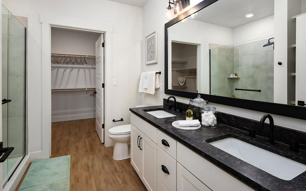 En-suite bath featuring walk-in glass shower, white cabinets, toilet, and doorway to spacious closet