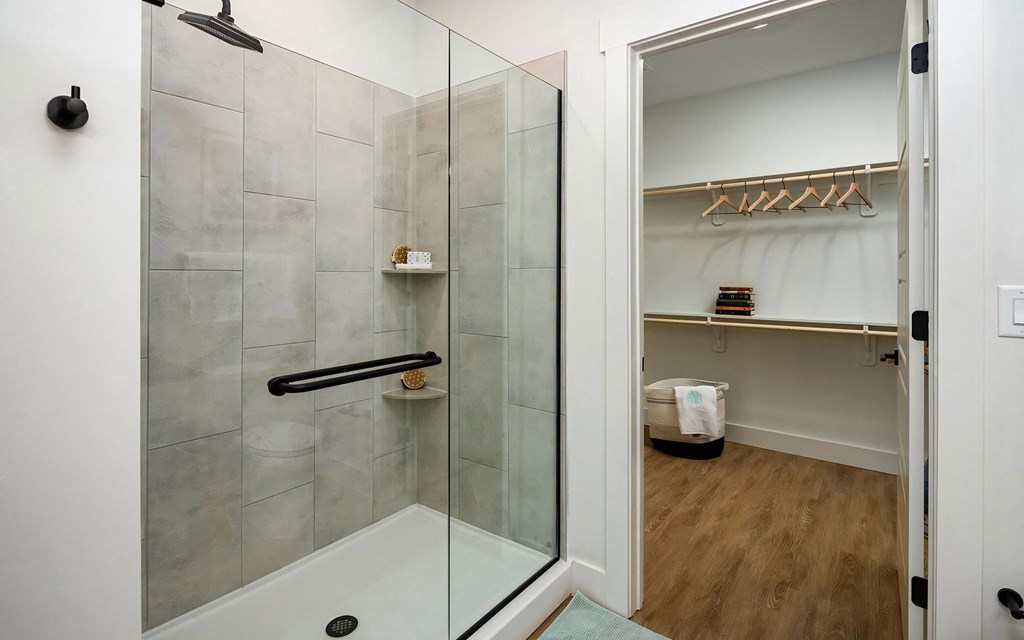 Bathroom features enclosed glass shower and open closet space with hangers and built-in shelving