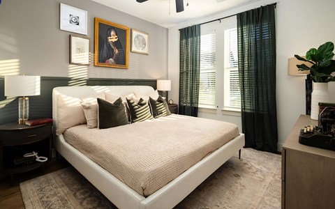 Bedroom with a deep green panel along the lower wall, upholstered platform bed, framed art, and two curtained windows.