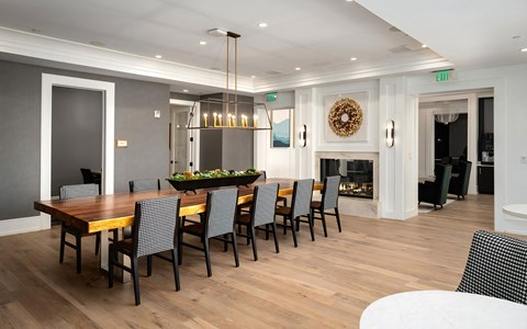 Dining room with a long live-edge wood table seating twelve, houndstooth chairs, a linear chandelier, and a fireplace.