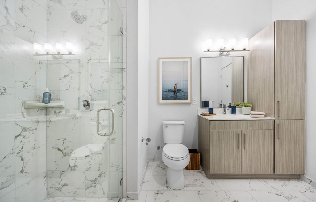 A bathroom with a marble shower, toilet, and sink.