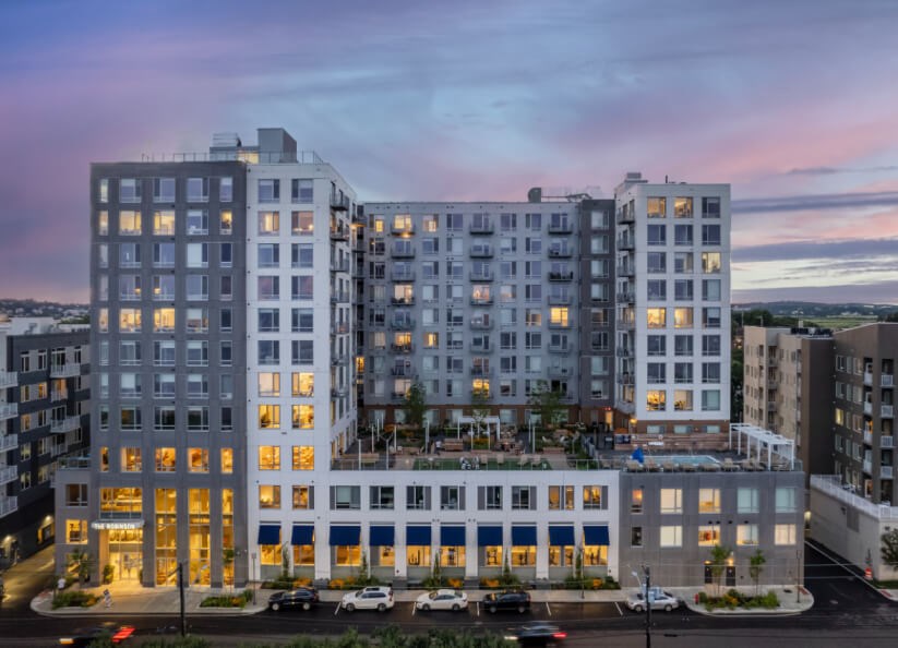 A large, modern apartment building with multiple balconies and a parking lot in front.