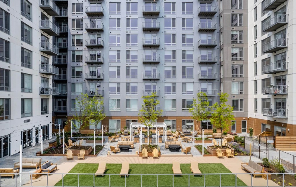 A large grassy area with benches and a pavilion is surrounded by apartment buildings.