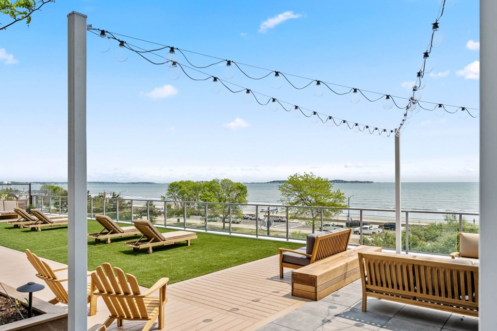 A wooden deck with chairs and a bench overlooking the water.
