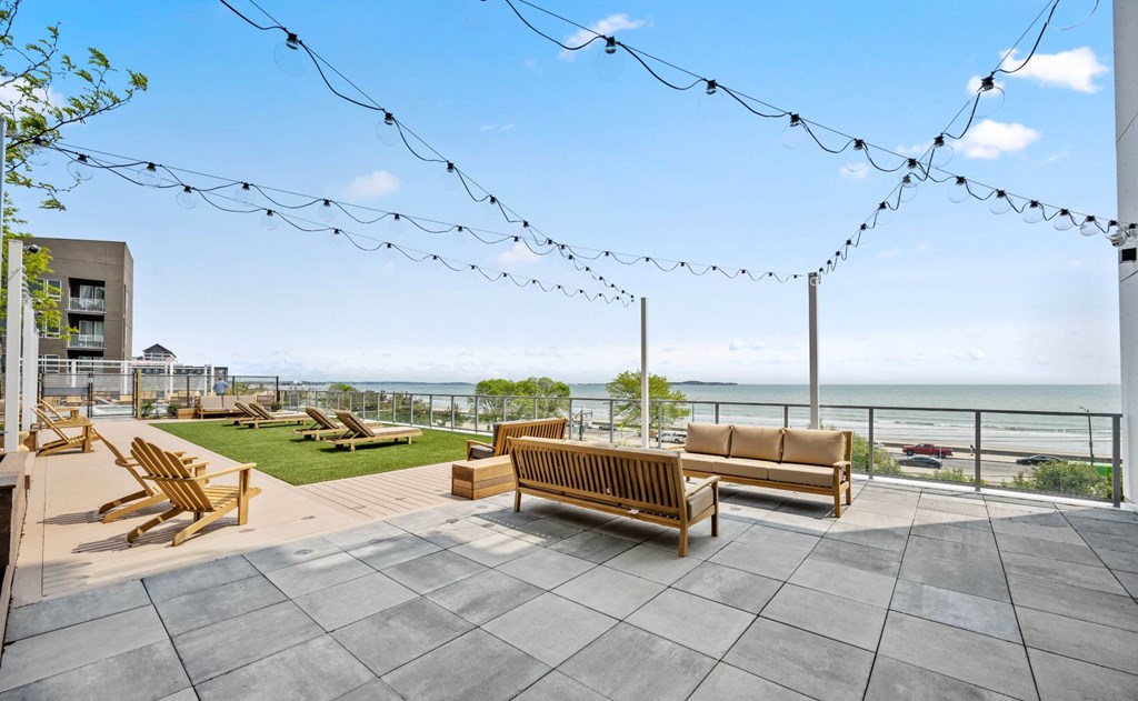 A patio with wooden furniture and string lights overlooking the ocean.