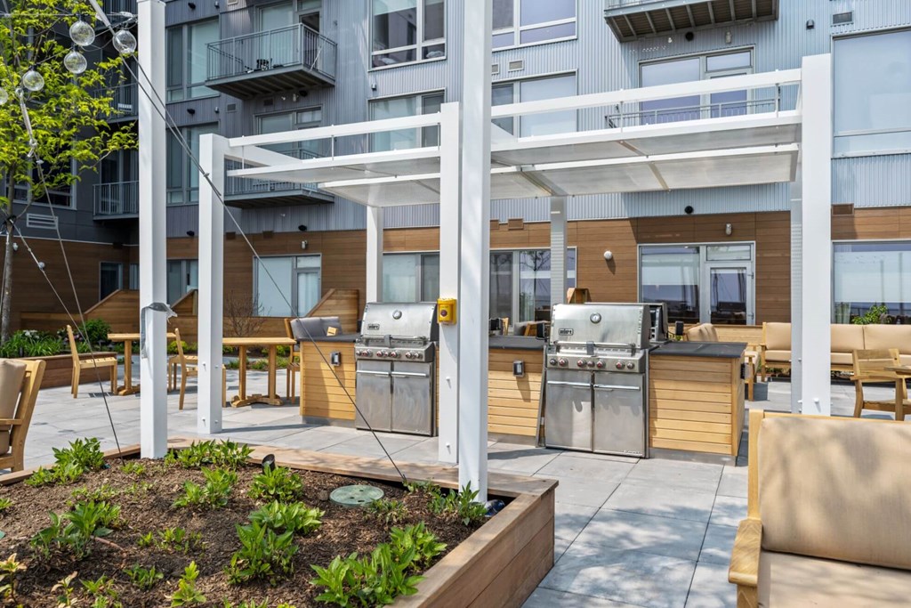 A patio with a grill and chairs is surrounded by a building.