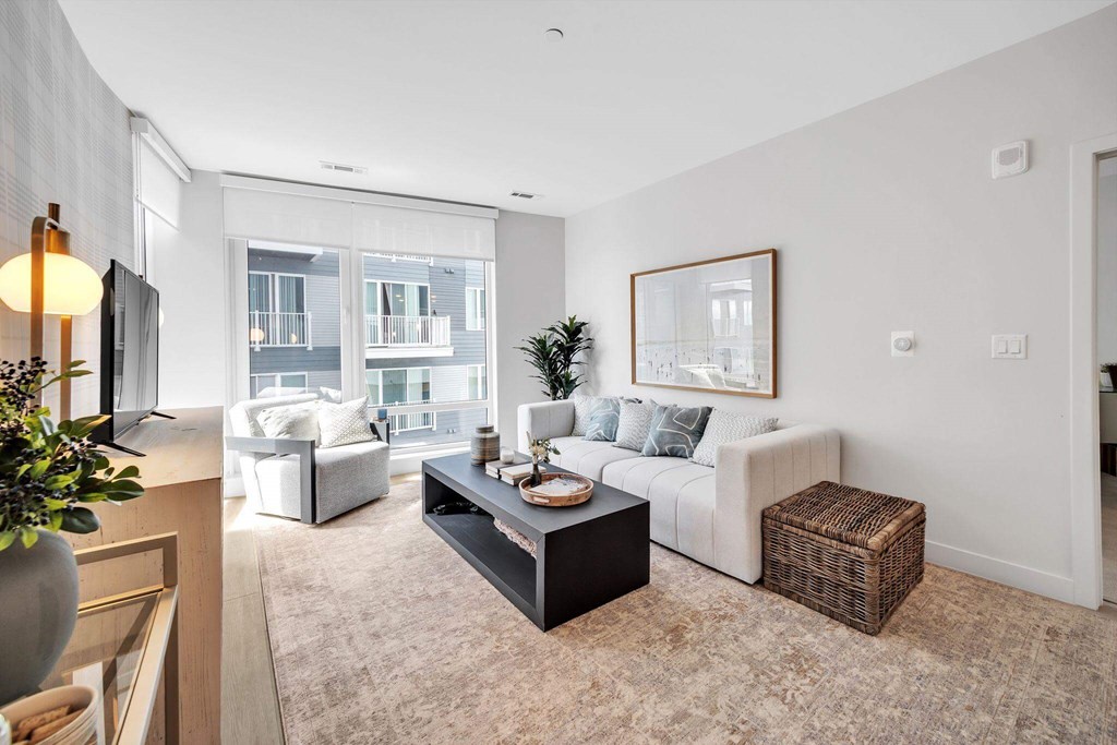 A living room with a white couch, a coffee table, and a large window.