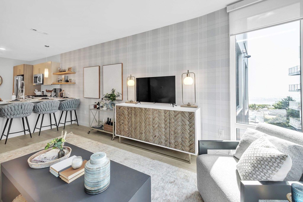 A modern living room with a grey sofa, a grey coffee table, a grey rug, a grey chair, a grey wall, a grey floor, a grey cabinet, a grey counter, a grey chair, a grey wall, a grey floor