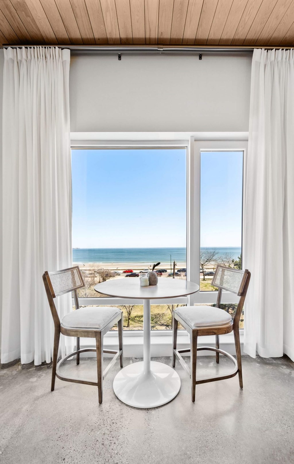 A dining table with chairs is set up by a window with a view of the beach.
