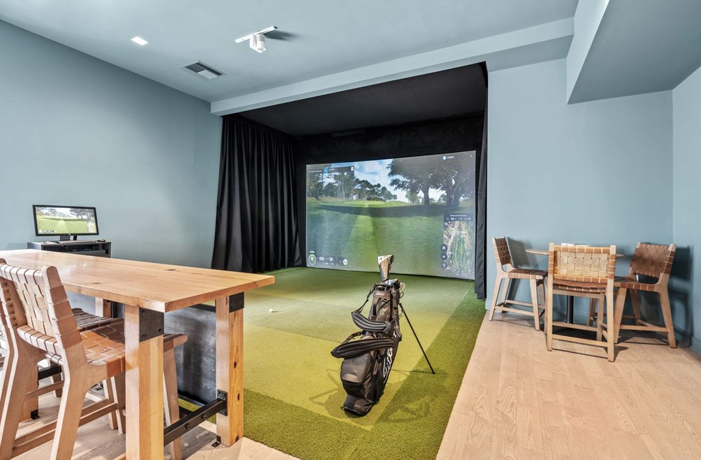 A room with a golf simulator and a table with chairs.