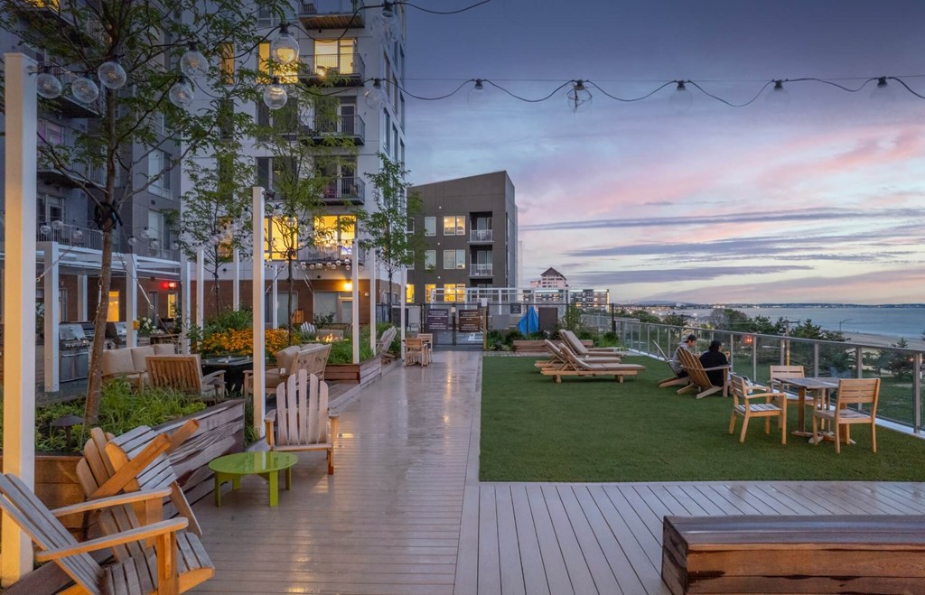 A rooftop patio with wooden furniture and string lights.