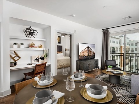 Dining table set for four beside a built-in desk and shelving niche, with a glass balcony door off to the right.