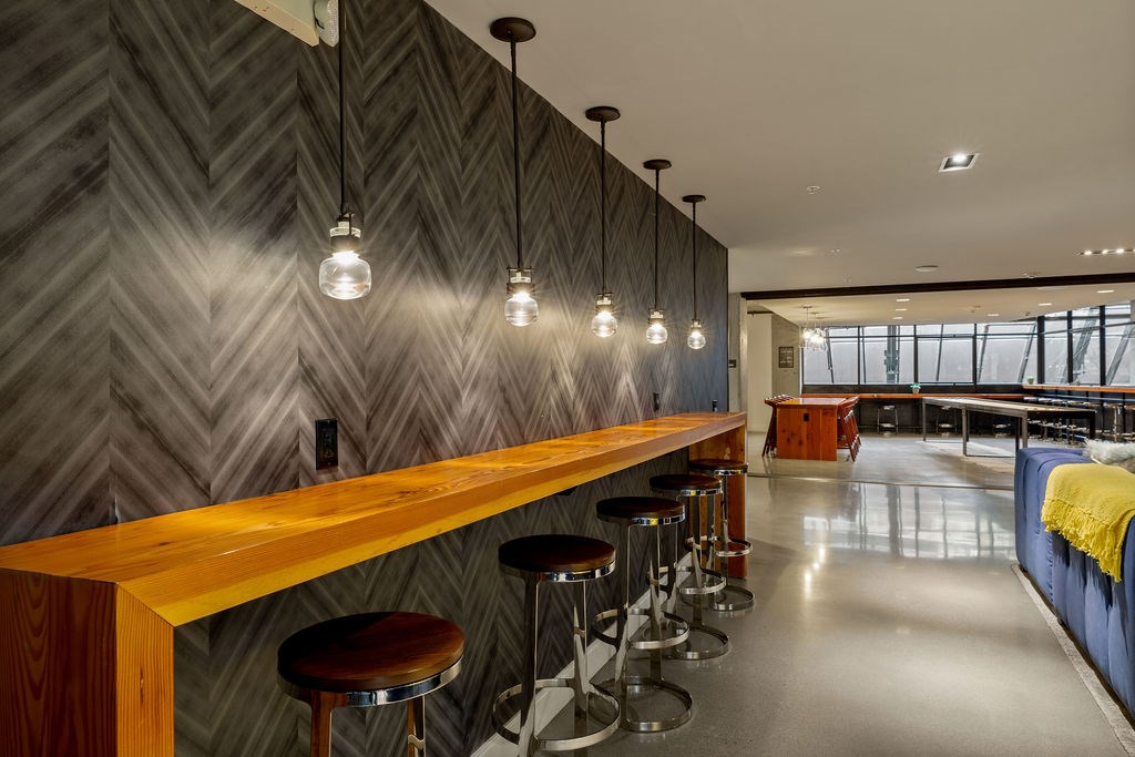 A long wooden bar with stools and pendant lights.