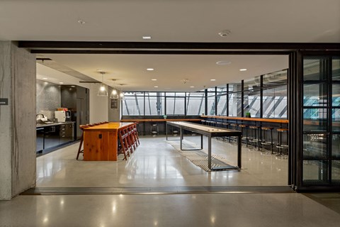 Community room seen through open glass doors, with a wood island, a shuffleboard table and a window bar beyond.