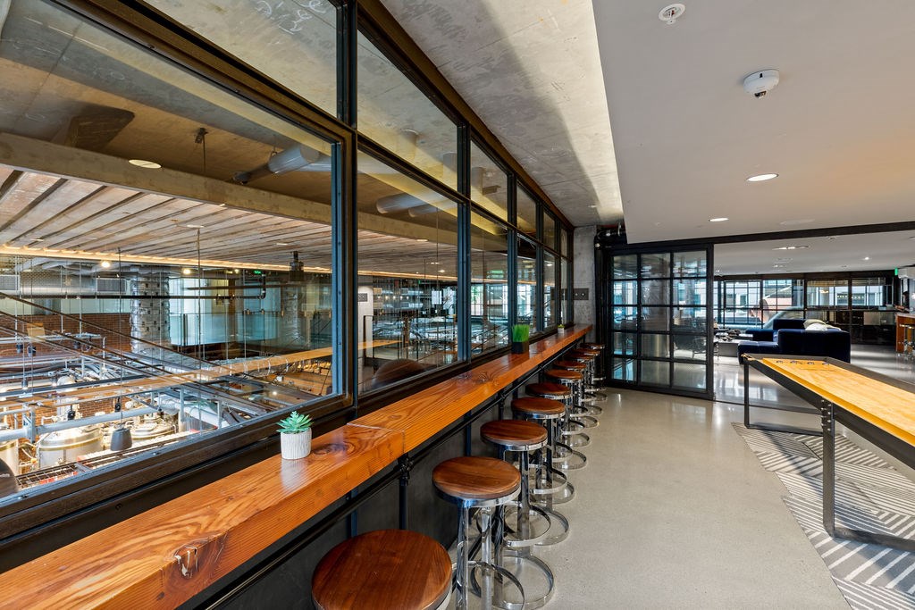 A long wooden bar with stools in front of a glass wall.
