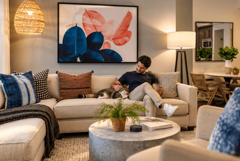 A man is sitting on a couch in a living room with a large abstract painting on the wall behind him.