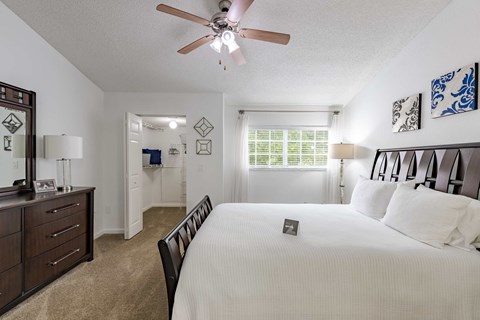 Bedroom with a ceiling fan, dark wood bed, dresser, and bathroom doorway.