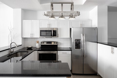 A modern kitchen with a stainless steel refrigerator and black countertops.