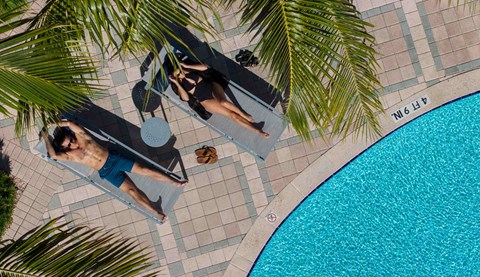 Two people relax on lounge chairs beside the swimming pool.