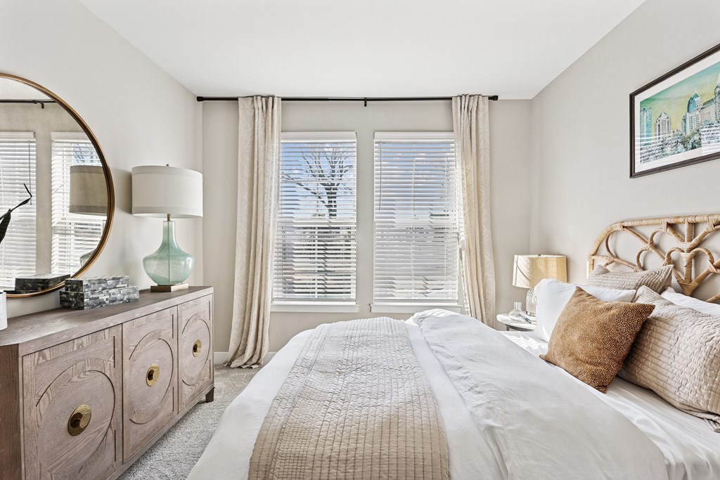 A bedroom with a large bed, a dresser with a mirror, and a window with blinds.