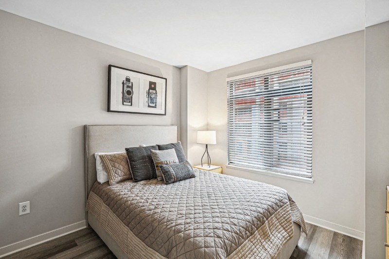 Bedroom with Bed, Lamp, and Window Blinds Overlooking Exterior