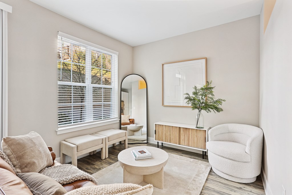 A living room with a white chair, a white sofa, a white coffee table, a white rug, a white wall, a white window with white blinds, a white floor, a white ceiling, a white picture frame, a white