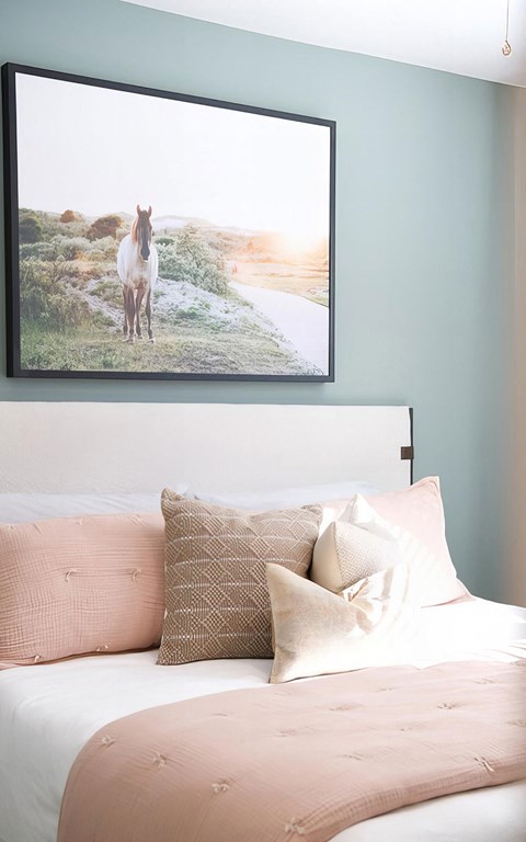 Bed made up in blush linens against a painted sage accent wall, with a large framed landscape photograph above it.