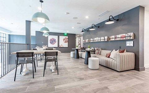 Reading lounge with a long cream sofa, a wall ledge of magazines, marble cafe tables and dome pendants overhead.