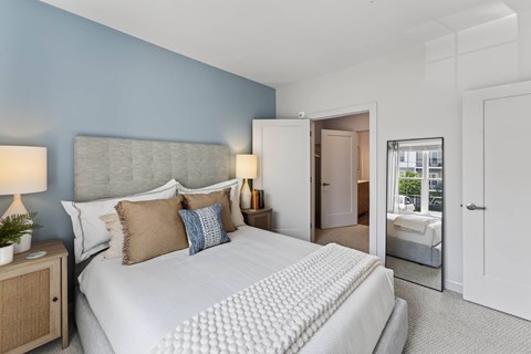 Bedroom with a blue accent wall and a tall leaning mirror, opening to a closet and an attached tiled bathroom.