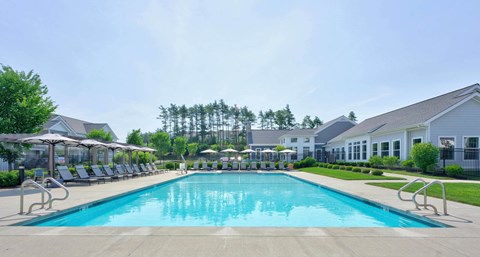 Rectangular pool seen down its full length, with umbrellas, loungers, clipped hedges and the clubhouse behind.