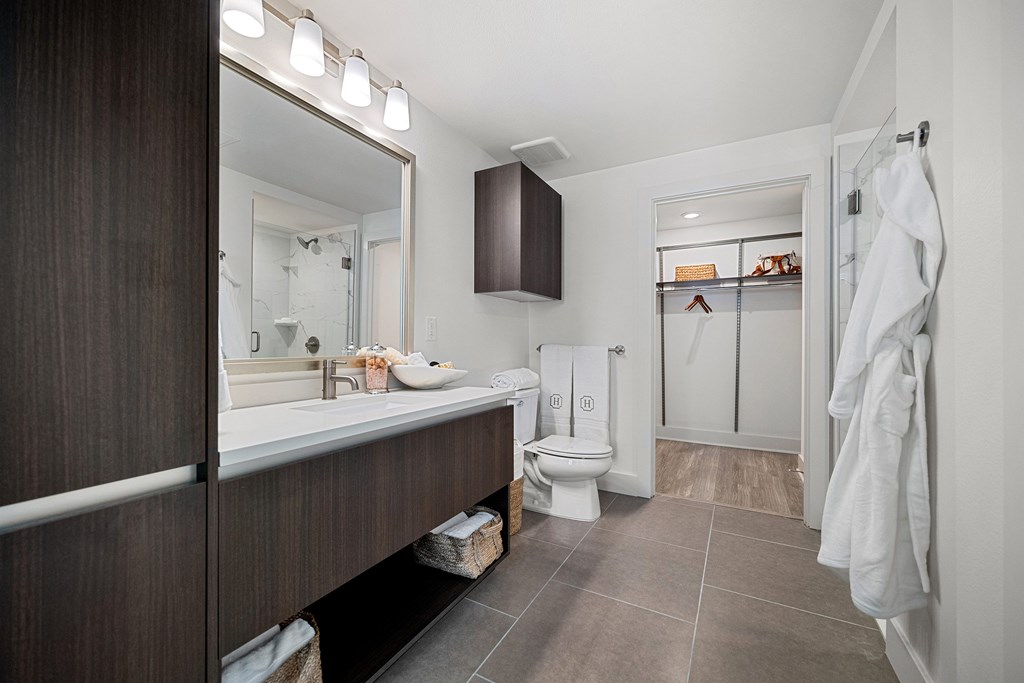 Spa-inspired bathroom offering a dual vanity, rich cabinetry, and direct access to a spacious walk-in closet