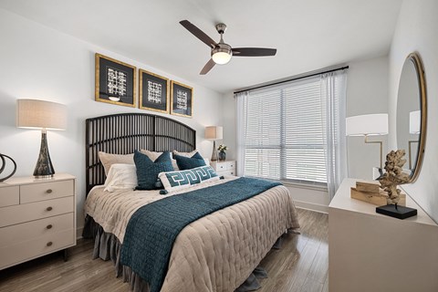 Bedroom with a dark spindle headboard, a ceiling fan, two nightstands and a tall window with blinds and curtains.