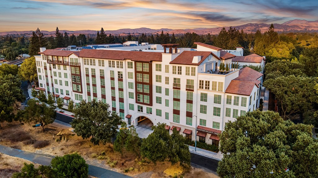 Sunset view of a Mediterranean-style apartment residence surrounded by rolling hills and natural beauty