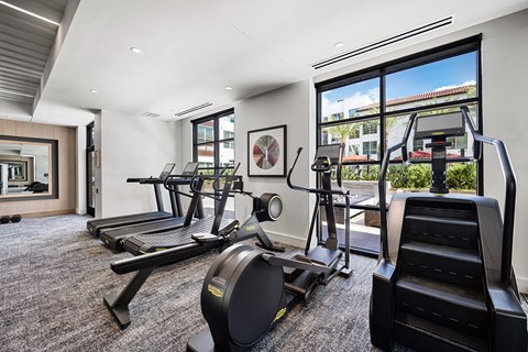 Cardio room with three treadmills, an elliptical and a stair climber facing a picture window onto the courtyard.
