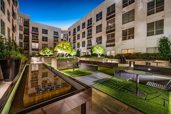 Courtyard game lounge with illuminated shuffleboard table, greenery, and intimate seating under the night sky