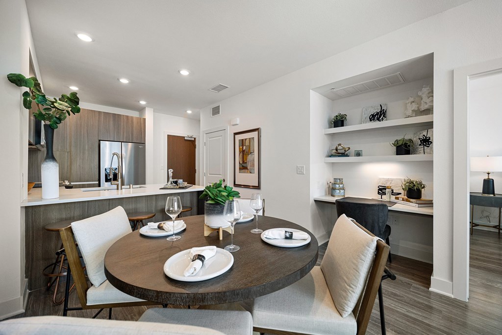 Dining area with a round table beside built-in shelving and open views into the kitchen