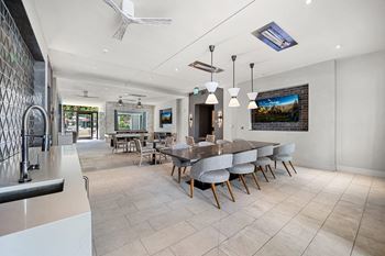 Clubroom with a long dining table, plush seating, and entertainment screens designed for community gatherings