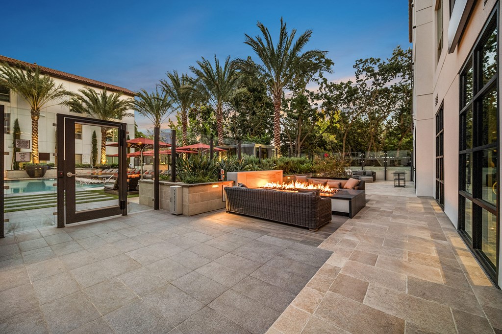 Fire pit lounge with woven seating, glowing flames, and palm-lined views creating a resort-style retreat