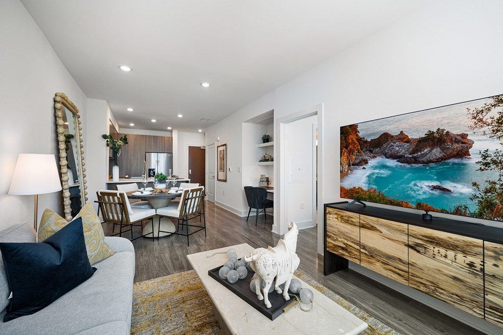 Bright living room with contemporary furnishings, wall-mounted TV, and open dining layout