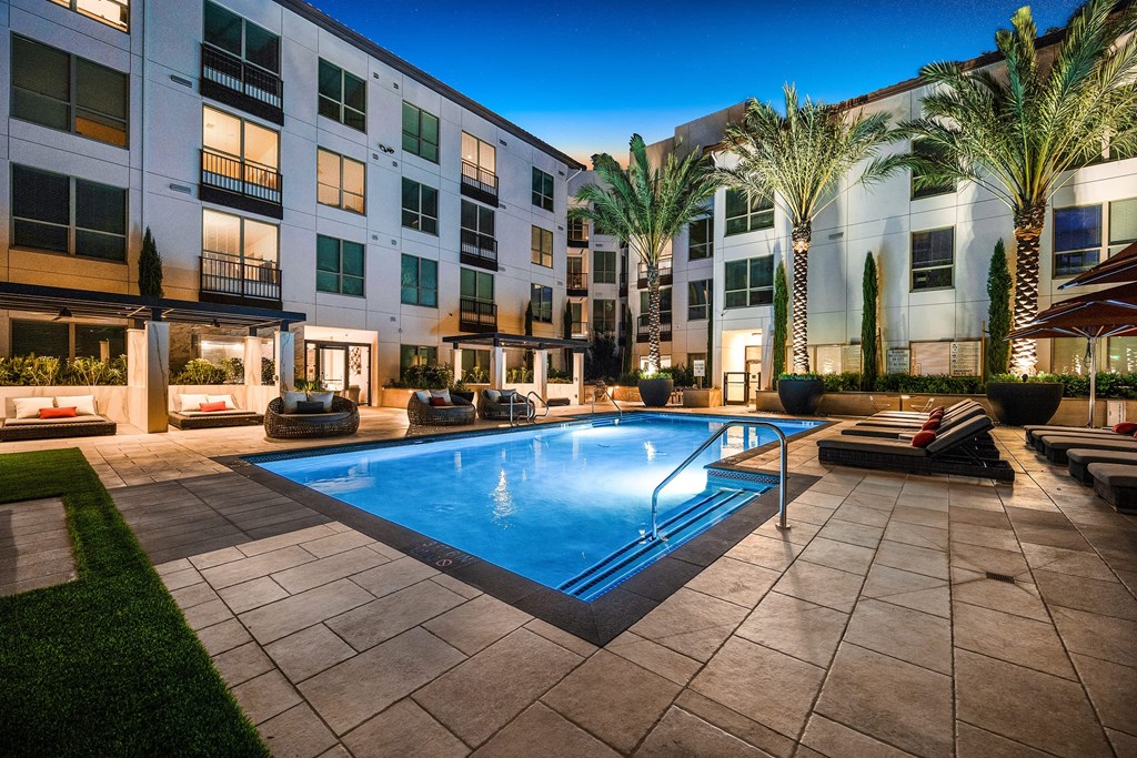 Tranquil pool surrounded by private cabanas, woven lounge chairs, and glowing palm trees
