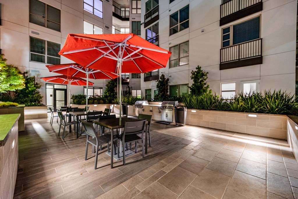 Outdoor dining area with grilling stations, red umbrellas, and modern seating for lively evenings with friends