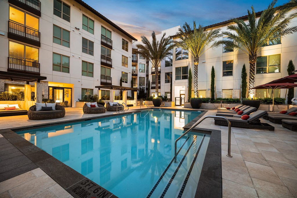 Sparkling pool surrounded by lounge seating, modern cabanas, and softly lit palm trees