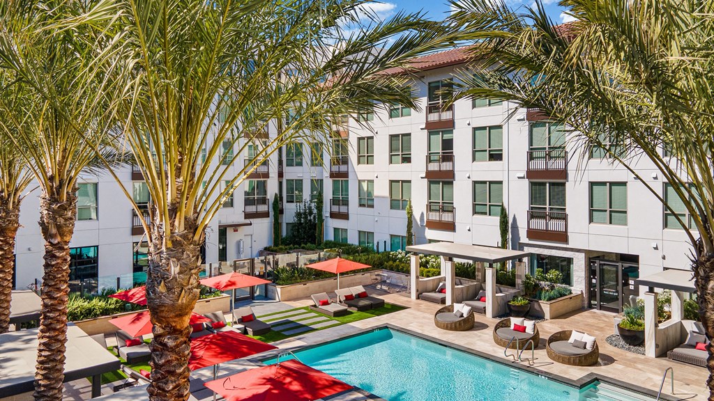 Resort-style pool courtyard with red umbrellas, palm trees, and private cabanas designed for relaxation and connection